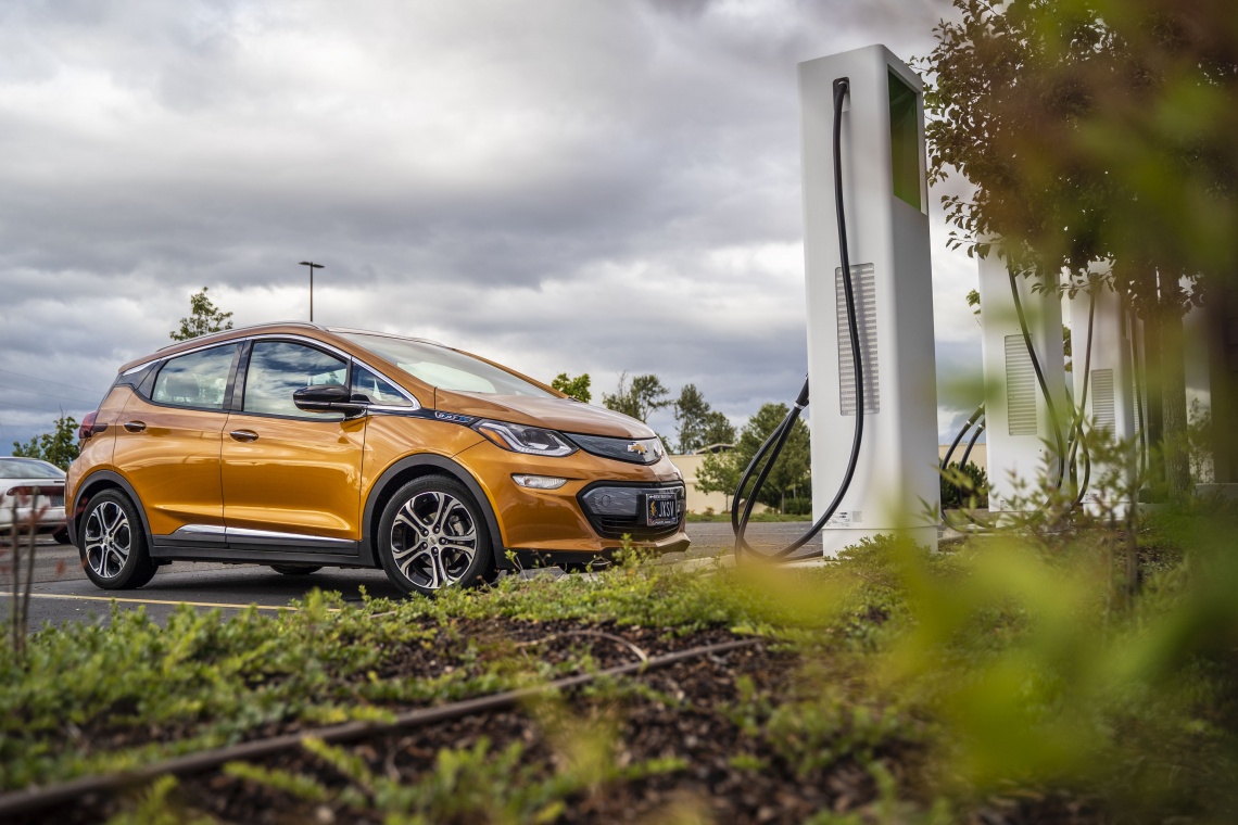 Orange colored Chevy Bolt at an outdoor charging station