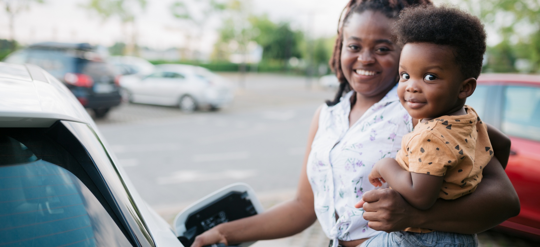 African American woman smiling while charging her car holding baby on her side
